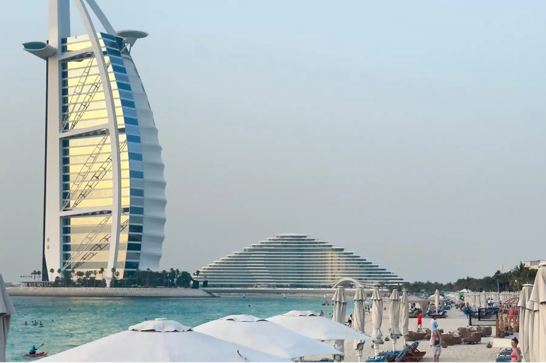Sunny beach with white umbrellas and the Burj Al Arab in the background, capturing daily life in Dubai