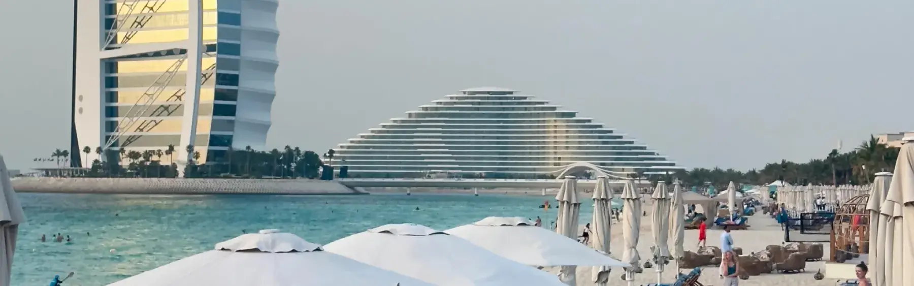 Sunny beach with white umbrellas and the Burj Al Arab in the background, capturing life in dubai