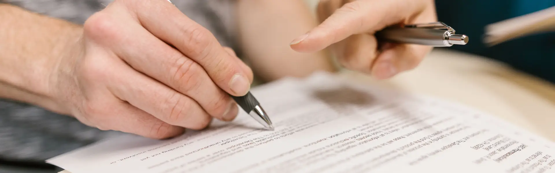 Close-up of two people signing a room rental contract example document on a table in a Dubai apartment, with a key and Emirates ID visible alongside the paperwork.